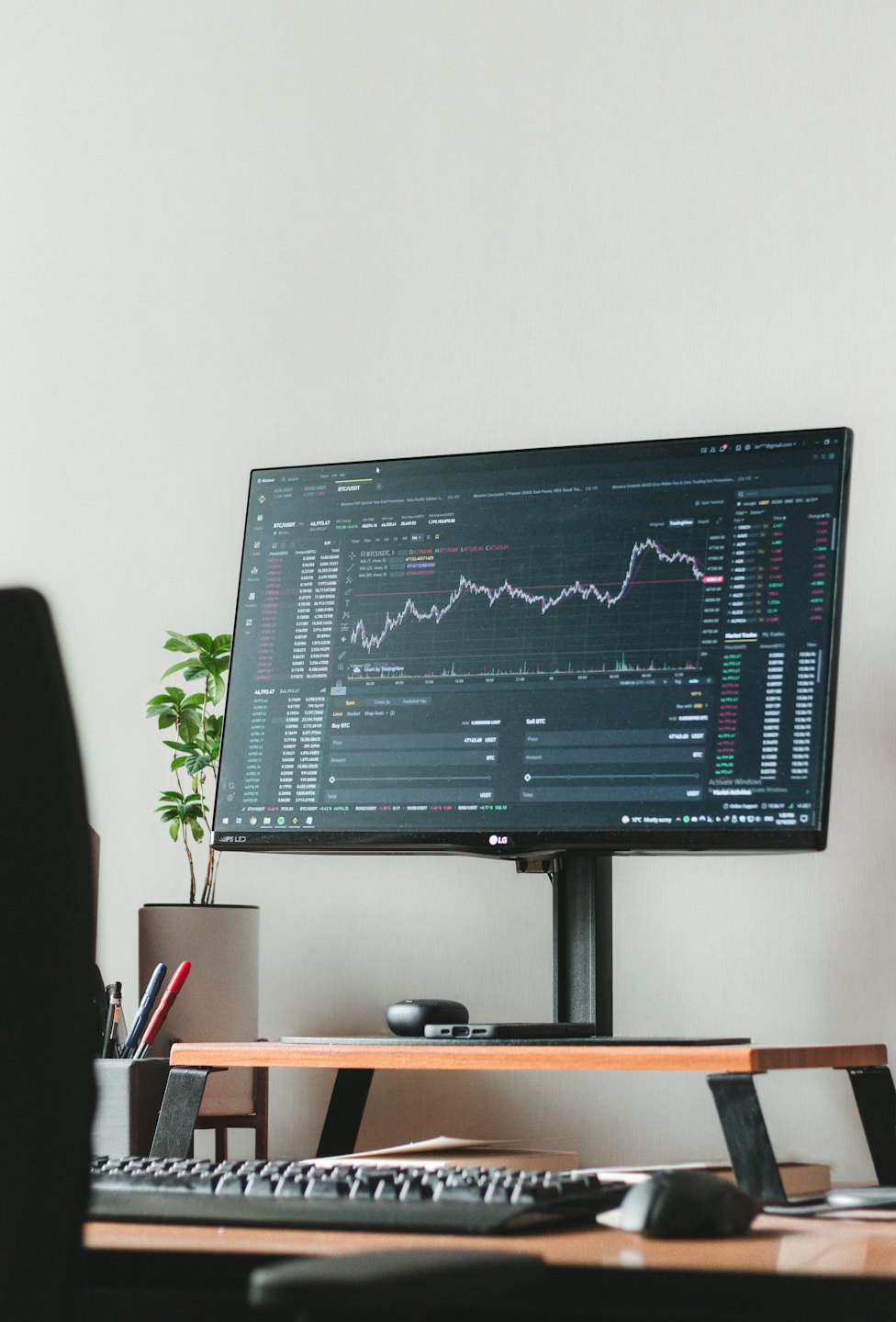 Computer monitor displays cryptocurrency charts on a minimalist desk.