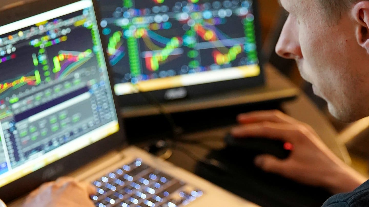Man using a laptop to analyze financial charts on multiple screens.